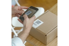 Holing a phone scanning a QR code on a cardboard box.